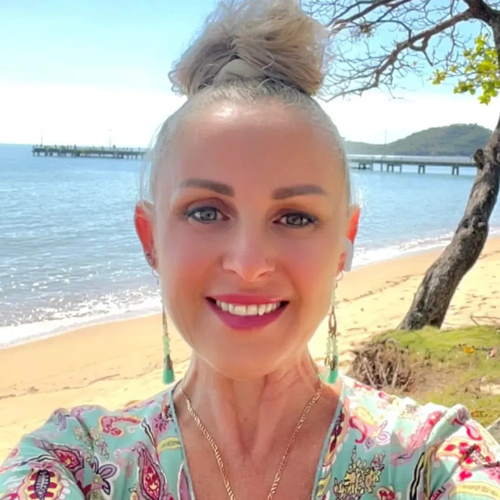 Mandy Magro in pastel-patterned top, with beach and pier in background. Bright sunny day.